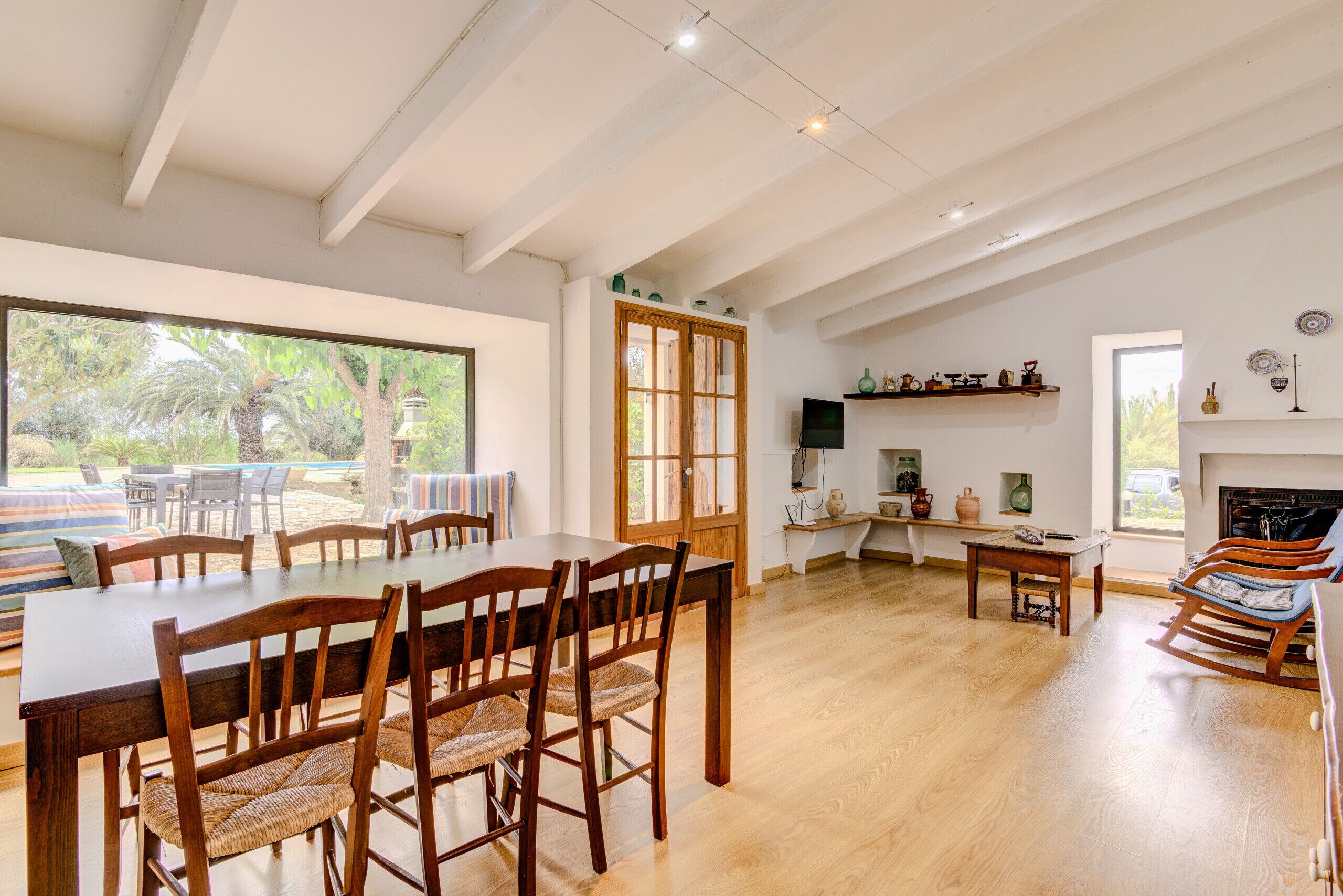 A spacious dining area with a large wooden table and chairs, a wooden ceiling, and a view of the outdoors.