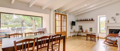 A spacious dining area with a large wooden table and chairs, a wooden ceiling, and a view of the outdoors.
