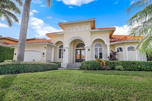 A Mediterranean-style house with a tiled roof, arched windows, and a well-maintained lawn.