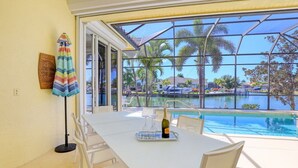 A dining area with a table set for two, a bottle of wine, and a glass set on a tray. - SW Exposure Home | Wide Canal w/ Pool & Spa (Marco Island)