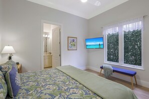 Un dormitorio con cama, un banco, un televisor y una ventana con vista a árboles.