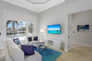 A modern living room with a large window, a flat-screen TV, a white sofa, and a glass coffee table.