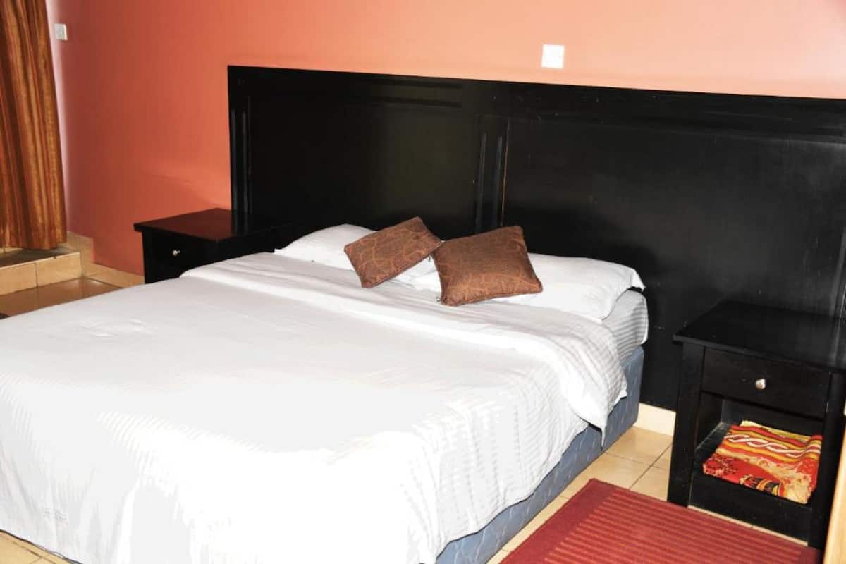 A neatly made bed with white bedding and two brown pillows, a black headboard, and a small bedside table with a red rug.