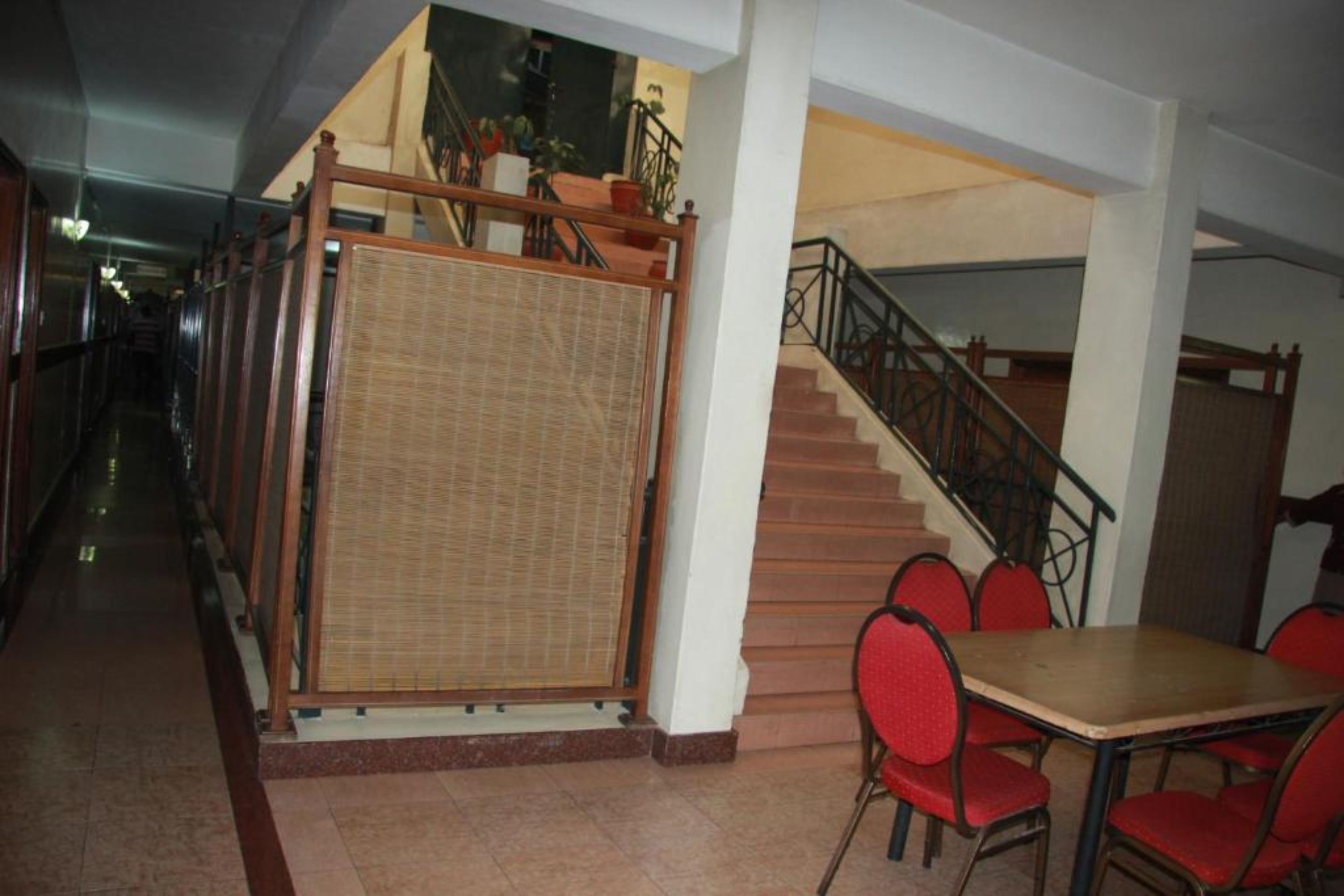 A hotel corridor with a staircase, a bamboo screen, and a dining area with red chairs.