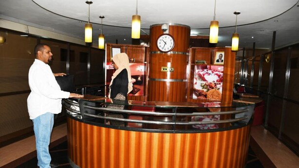 A reception area with a wooden counter, a clock, and a security camera. - Jamia Central Hotel (Nairobi)
