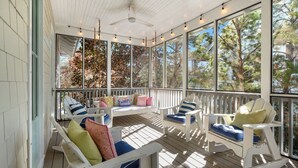 A covered porch with white wooden furniture, including rocking chairs and a bench, with large windows offering views of trees and a house. - Southern Tide - WaterColor Park District, Complimentary 6 - Seater Golf Cart! (Santa Rosa Beach)