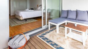 A modern hotel room with a bed, a sofa, a small table, and a glass door leading to a balcony. - Quinta do Mar - Watch The Sun Rise Over The Ocean (Angra do Heroismo)