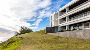 A modern building with a flat roof, multiple balconies, and a concrete retaining wall. - Quinta do Mar - Watch The Sun Rise Over The Ocean (Angra do Heroismo)