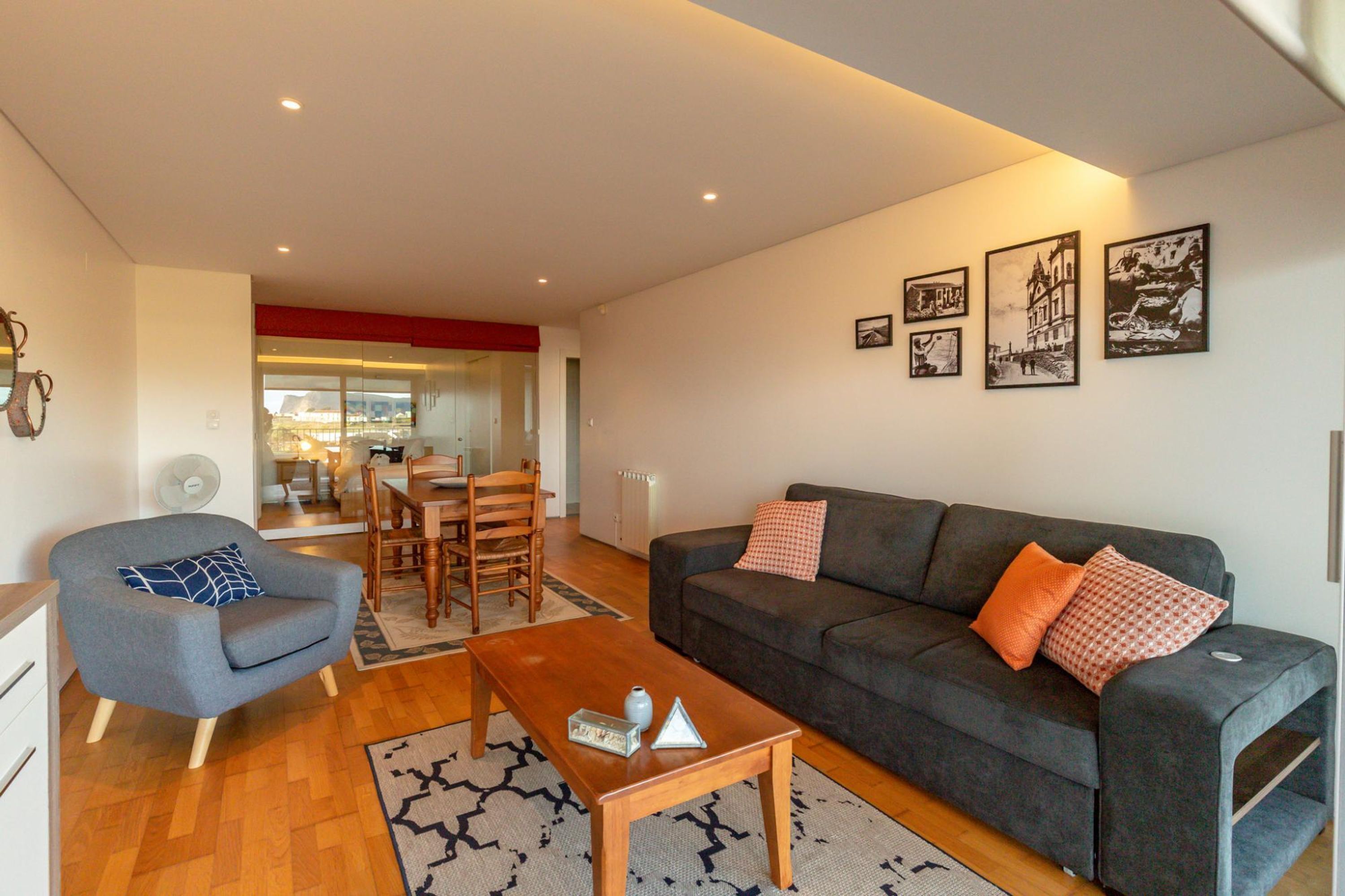 A modern living room with a grey sofa, a wooden coffee table, and a dining area with wooden chairs and a table.