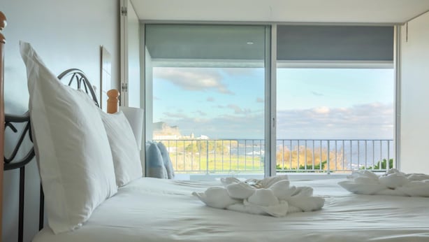 A hotel room with a bed, white pillows, and a view of a balcony with a railing. - Quinta do Mar - Watch The Sun Rise Over The Ocean (Angra do Heroismo)
