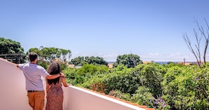 A couple standing on a balcony overlooking a lush garden and a coastal view. - Porto Tranquilo in Porto Martins (Praia da Vitoria)