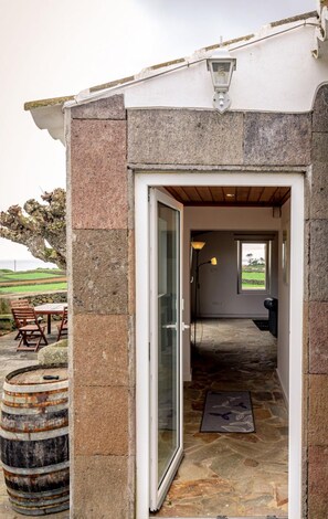 A stone building with a glass door entrance leading to a room with a window and a lamp. - Casa dos Cal os in S o Mateus da Calheta (Angra do Heroismo)