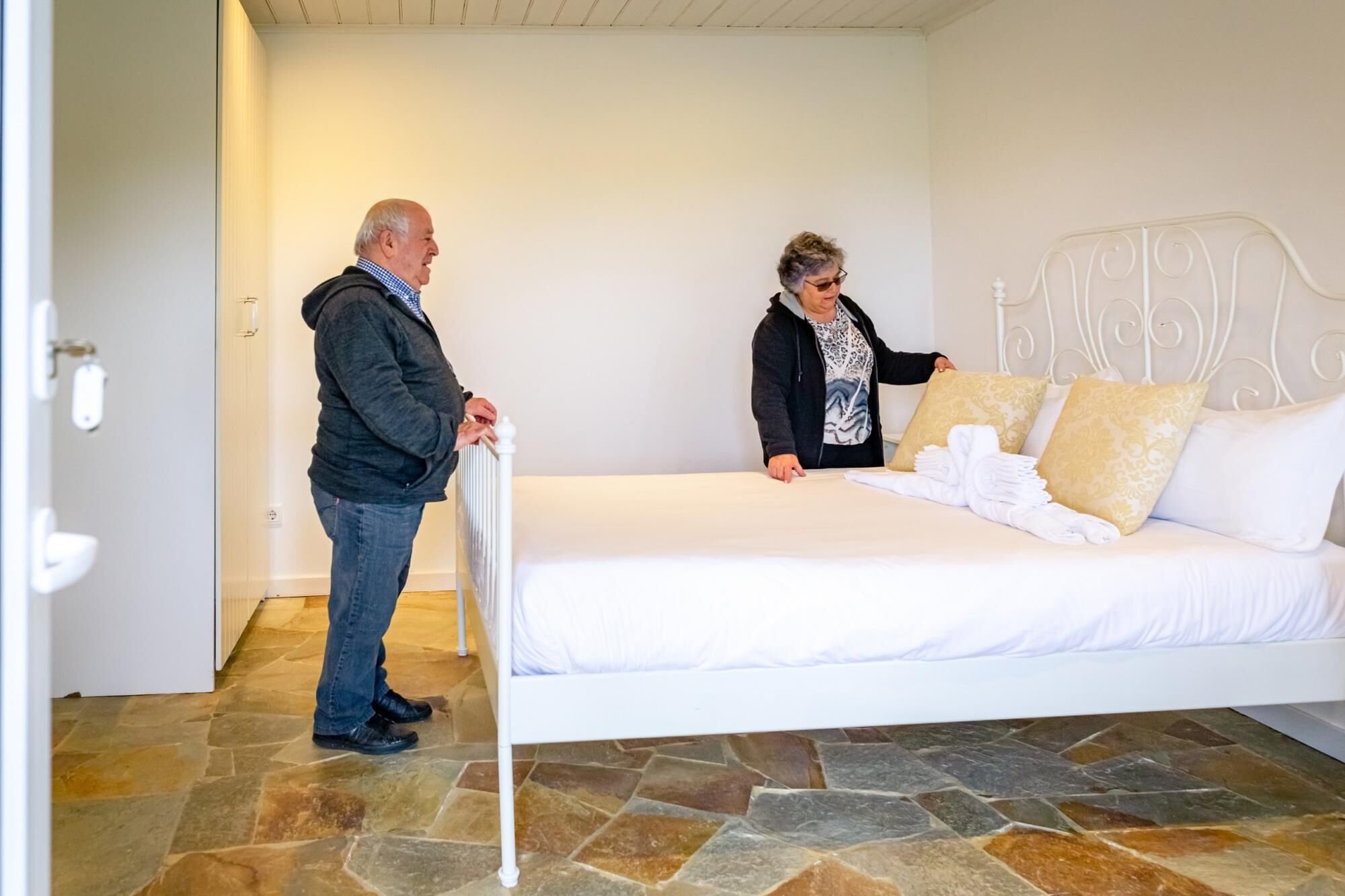 A bedroom with a white bed, stone flooring, and a metal headboard.