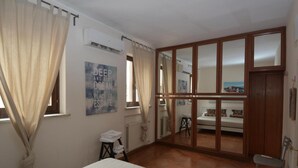 A bedroom with a bed, a radiator, a window with curtains, a wardrobe, and a mirror. - Piazza Navona Penthouse - Piazza Navona Penthouse (Rome)