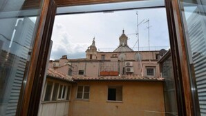A view through a window of a building with a tiled roof, a bell tower, and satellite dishes. - Piazza Navona Penthouse - Piazza Navona Penthouse (Rome)