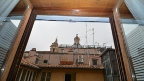 A view through a window of a building with two prominent towers, a balcony, and a satellite dish. - Piazza Navona Penthouse - Piazza Navona Penthouse (Rome)