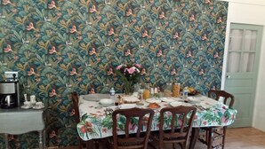 Comedor con mantel floral, sillas de madera y papel tapiz estampado.
