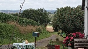 Entorno rural al aire libre con una mesa, sillas, un buzón y plantas en macetas.