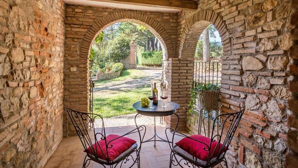 A stone-walled patio with two metal chairs and a table, a bottle of wine, and a basket of grapes. - Casa Ciculino 8 (Monteleone d'Orvieto)