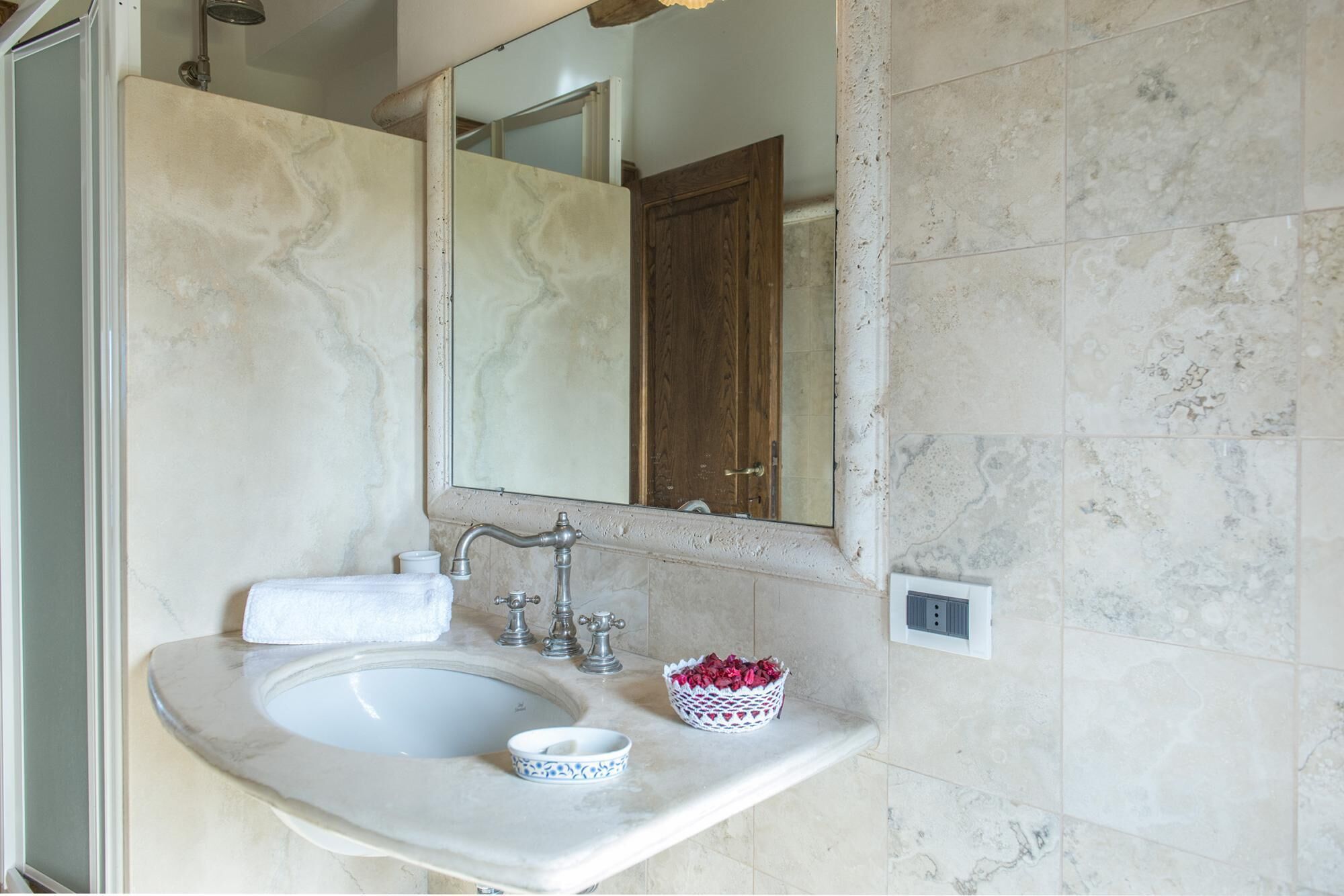 A bathroom with a marble sink, a wooden door, and a mirror.