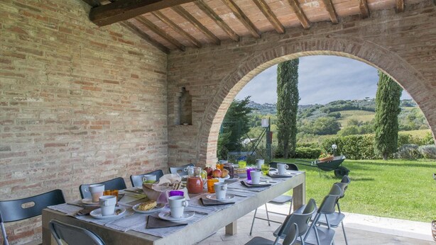 An outdoor dining area with a brick wall and an archway leading to a scenic view of hills and trees.