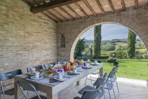 An outdoor dining area with a brick wall and an archway leading to a scenic view of hills and trees. - Casale Dei 12 in Montepulciano (Montepulciano)