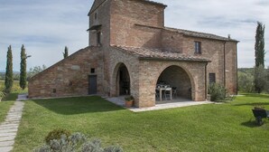 A rustic stone building with a central tower, arched doorways, and a paved courtyard.