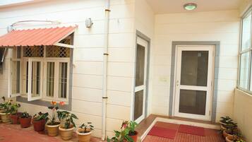 A building with a red roof, potted plants, a door with a glass panel, and a tiled floor.
