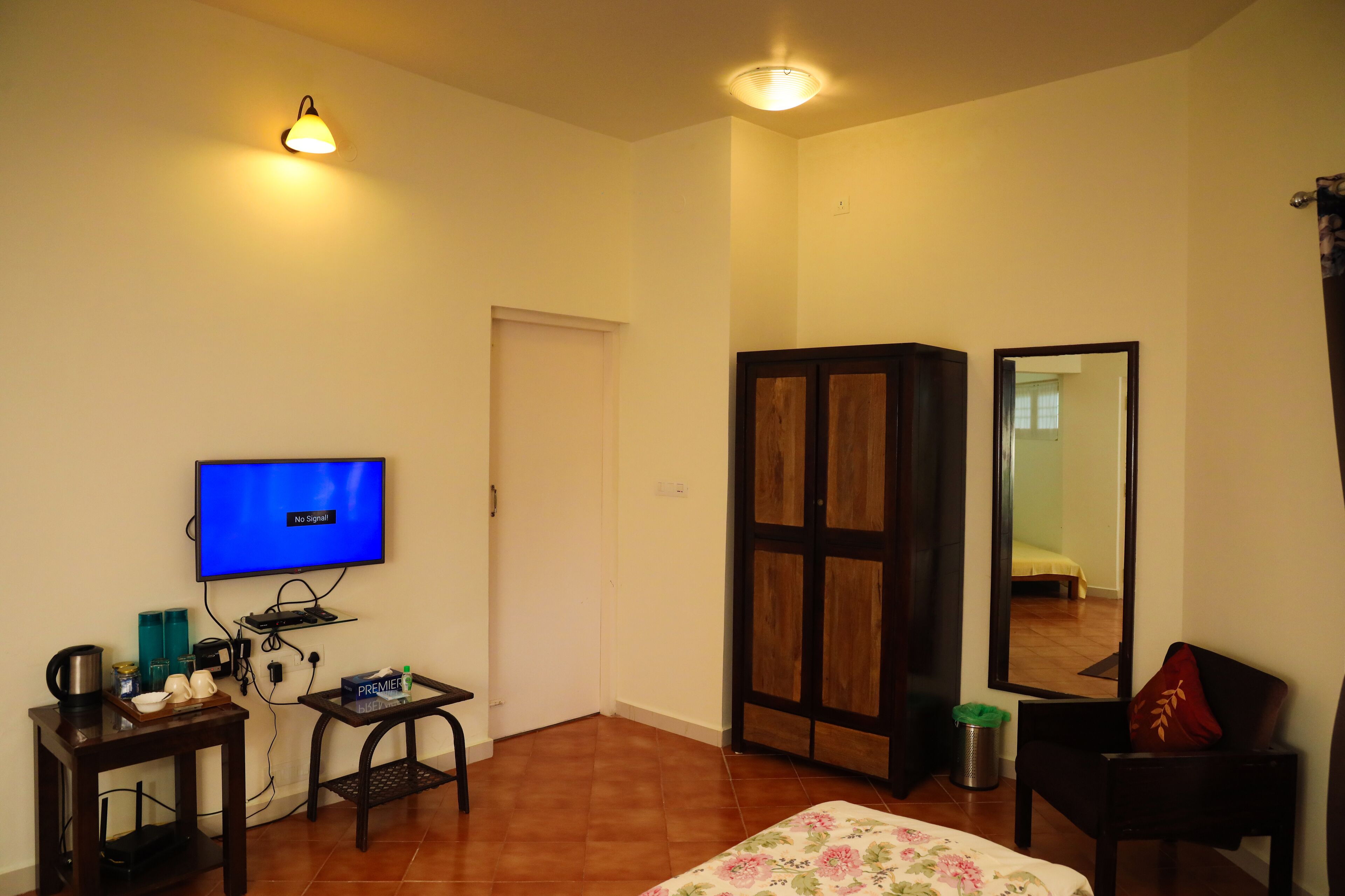 Habitación de hotel con televisión, una mesita con cafetera, un espejo y una cama con edredón estampado con motivos florales.