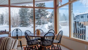 Un comedor con un amplio ventanal con vistas a un paisaje nevado, con una mesa de madera y sillas negras.