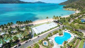 An aerial view of a resort with a swimming pool, beach, and palm trees.