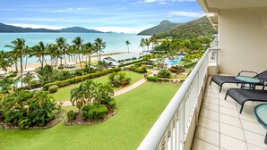 A balcony with a view of a beach, pool, and lush greenery.