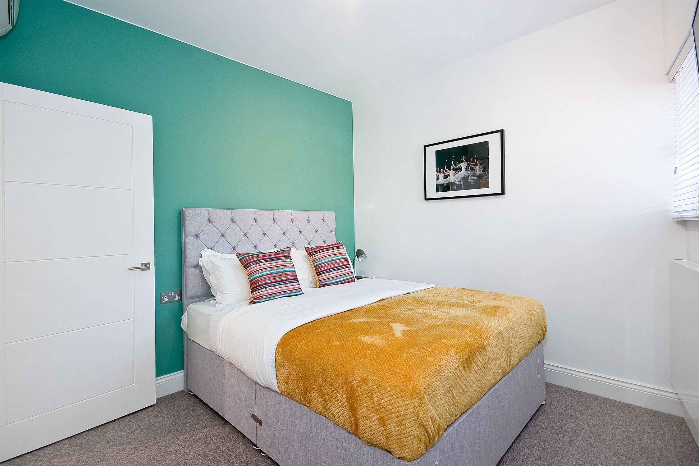 A bedroom with a bed, a white door, a teal wall, and a framed picture on the wall.