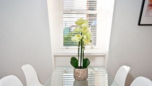 A dining table with a glass top, surrounded by white chairs, and a potted plant in the center. - Interlude House by City Living London (London)