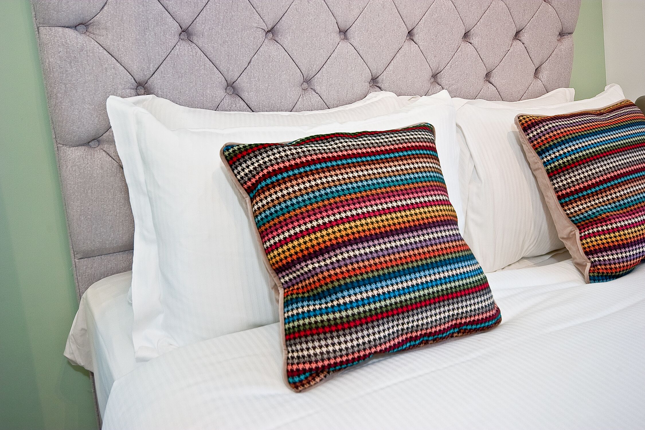 A bed with a tufted headboard and two colorful striped pillows.