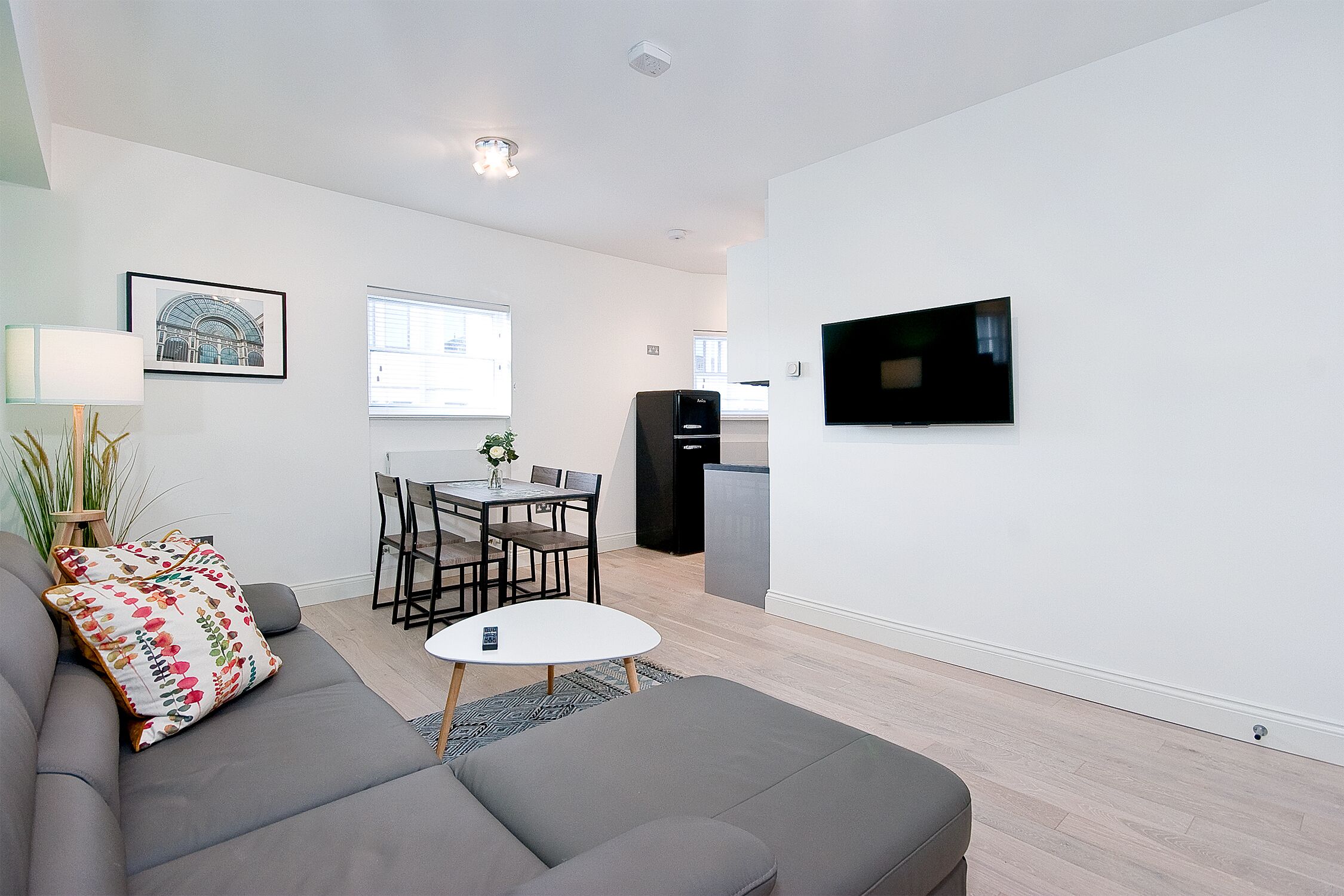 A modern living room with a grey sofa, a small round table, and a TV mounted on the wall.