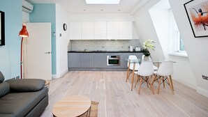 A modern kitchen with white cabinets, a skylight, and a dining area with a glass table and white chairs. - Interlude House by City Living London (London)