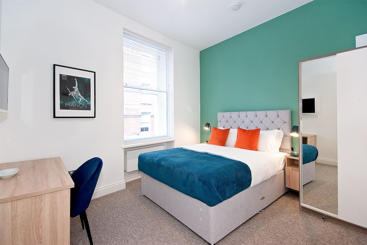 Un dormitorio moderno con cama, mesita de noche y espejo.