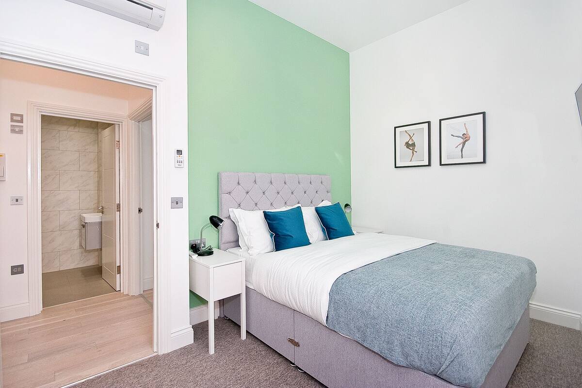 Un dormitorio con cama, mesita de noche y puerta de baño.
