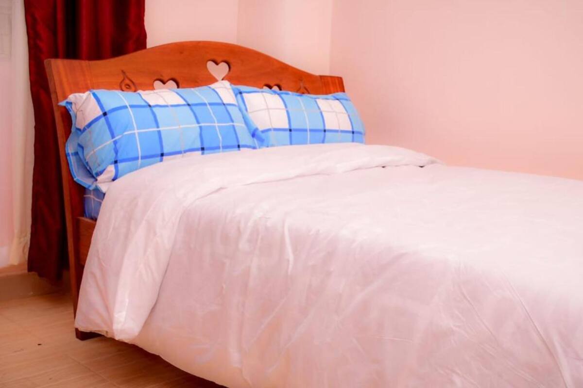 Ein Bett mit Holz-Kopfteil, Kissen in blau-weiß kariertem Muster und einer weißen Decke.
