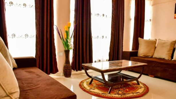 A living room with a sofa, a coffee table, a vase with flowers, and a patterned rug. - Faraja Guest House (Naivasha)