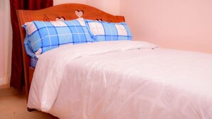 A single bed with a wooden headboard, a white duvet, and blue and white checkered pillows. - Faraja Guest House (Naivasha)