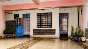 A spacious lobby with a patterned floor, two blue doors, a large window with a grid pattern, and a stone wall. - Faraja Guest House (Naivasha)