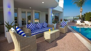 A modern outdoor lounge area with wicker furniture and striped cushions, overlooking a swimming pool and a clear blue sky. - Protaras holiday villa - rentprivatevillas 113 (Protaras)