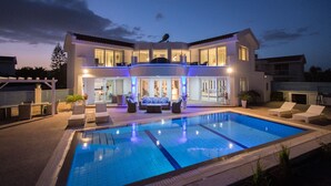 A modern two-story house with a swimming pool, outdoor seating, and a well-lit entrance. - Protaras holiday villa - rentprivatevillas 113 (Protaras)