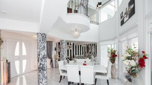 A spacious, well-lit interior with a dining area, a large column, and a staircase leading to an upper level. - Protaras holiday villa - rentprivatevillas 113 (Protaras)