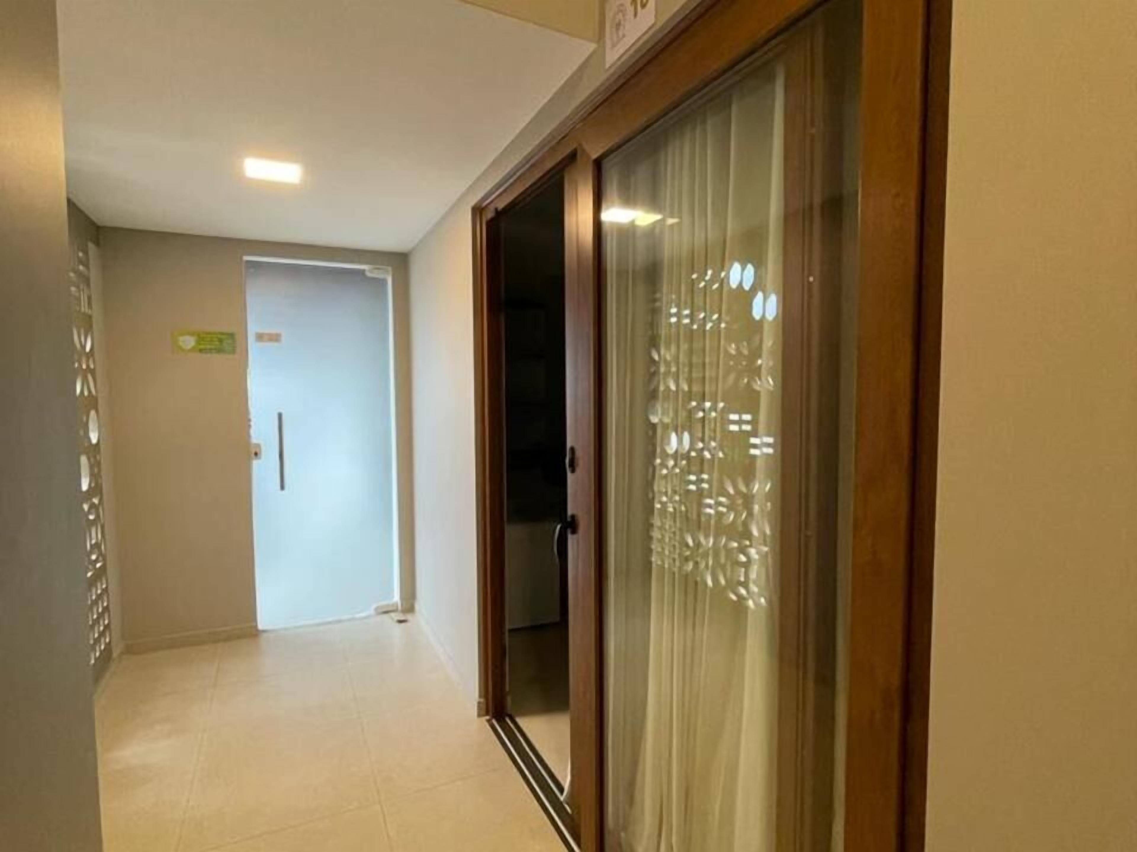 A hallway with a sliding glass door leading to a room. The hallway has a tiled floor and a door with a sign above it.