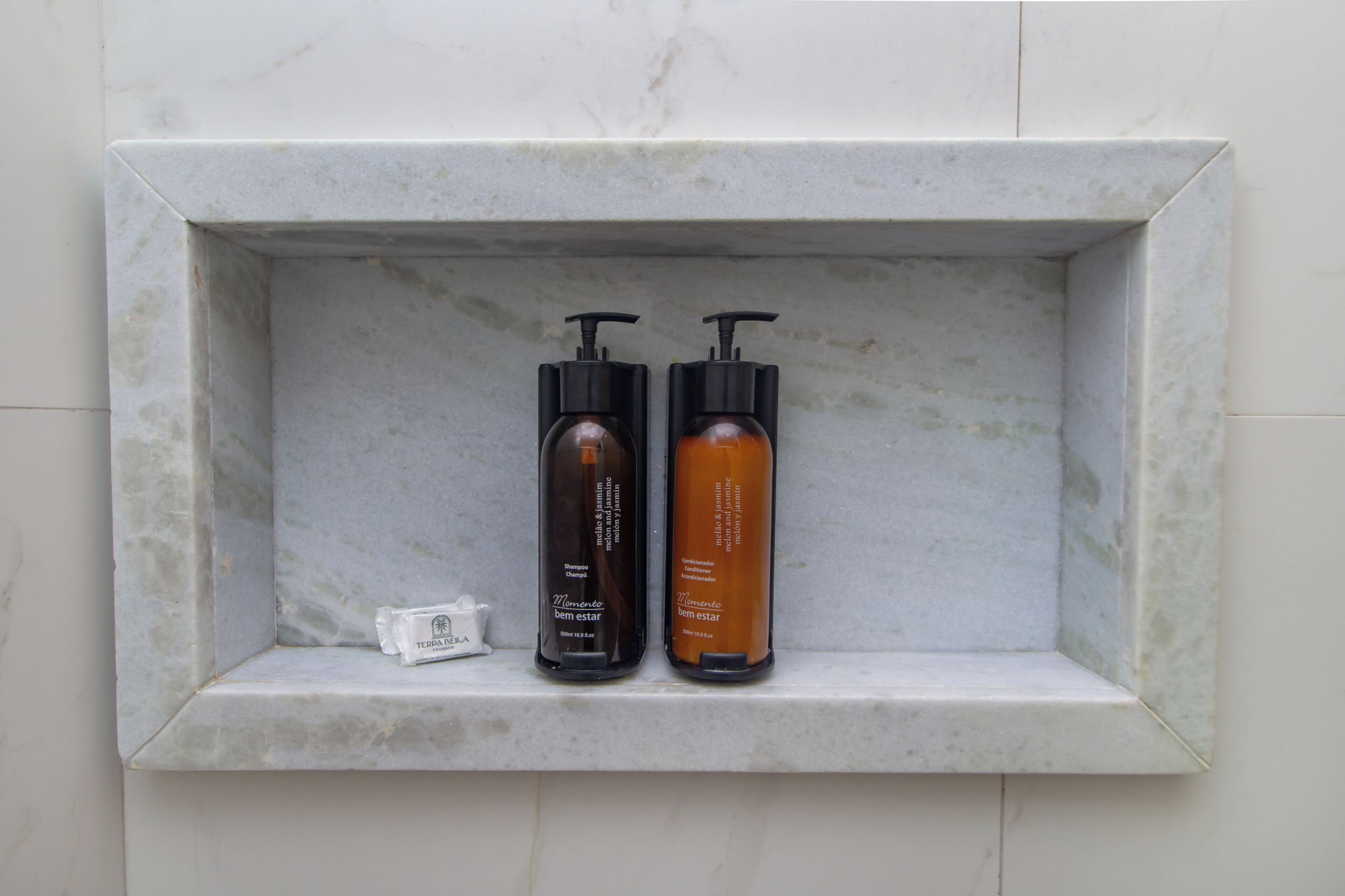 A bathroom shelf with two bottles of shampoo and a soap dispenser.