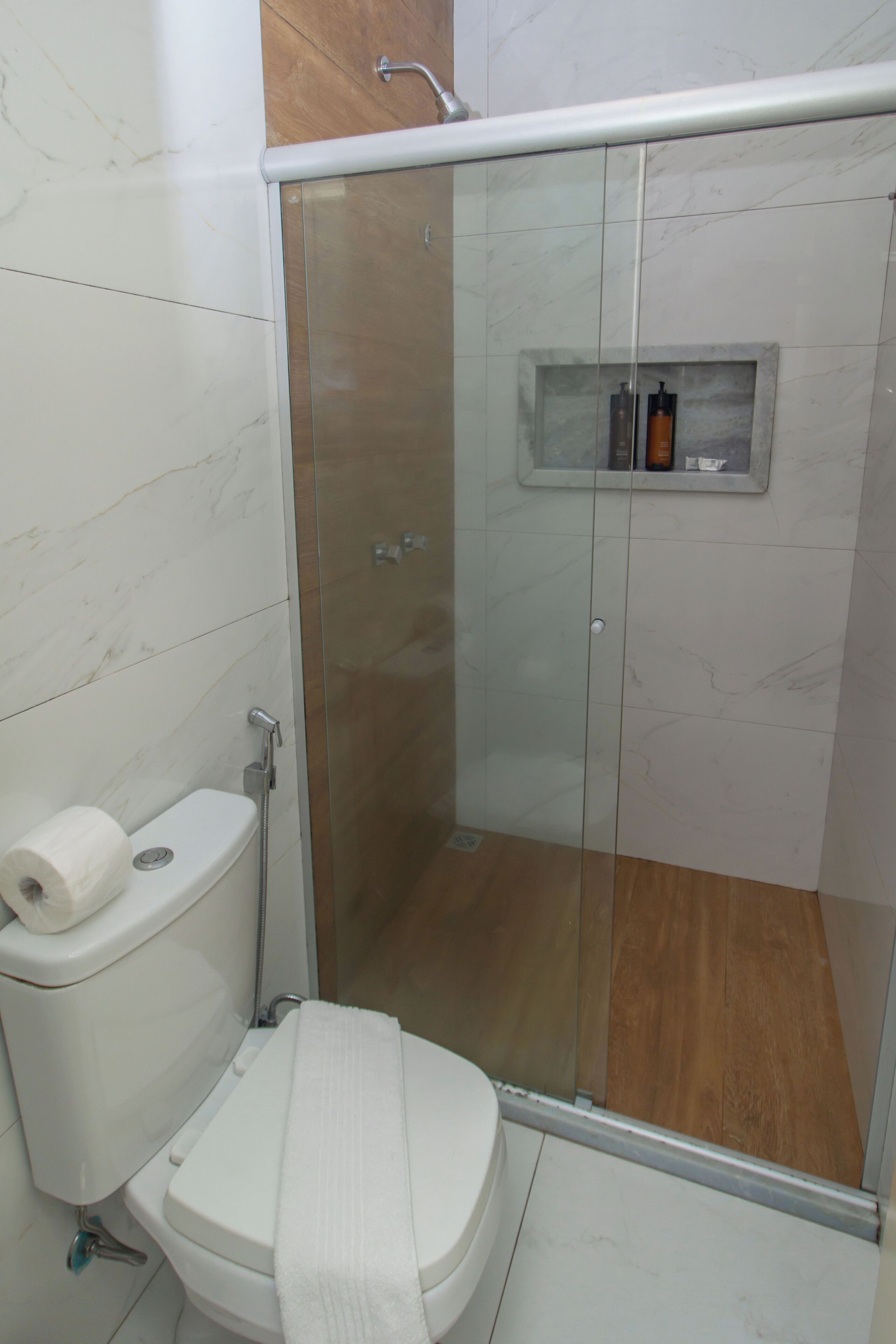 A bathroom with a toilet, a shower enclosure, and a shelf with toiletries.