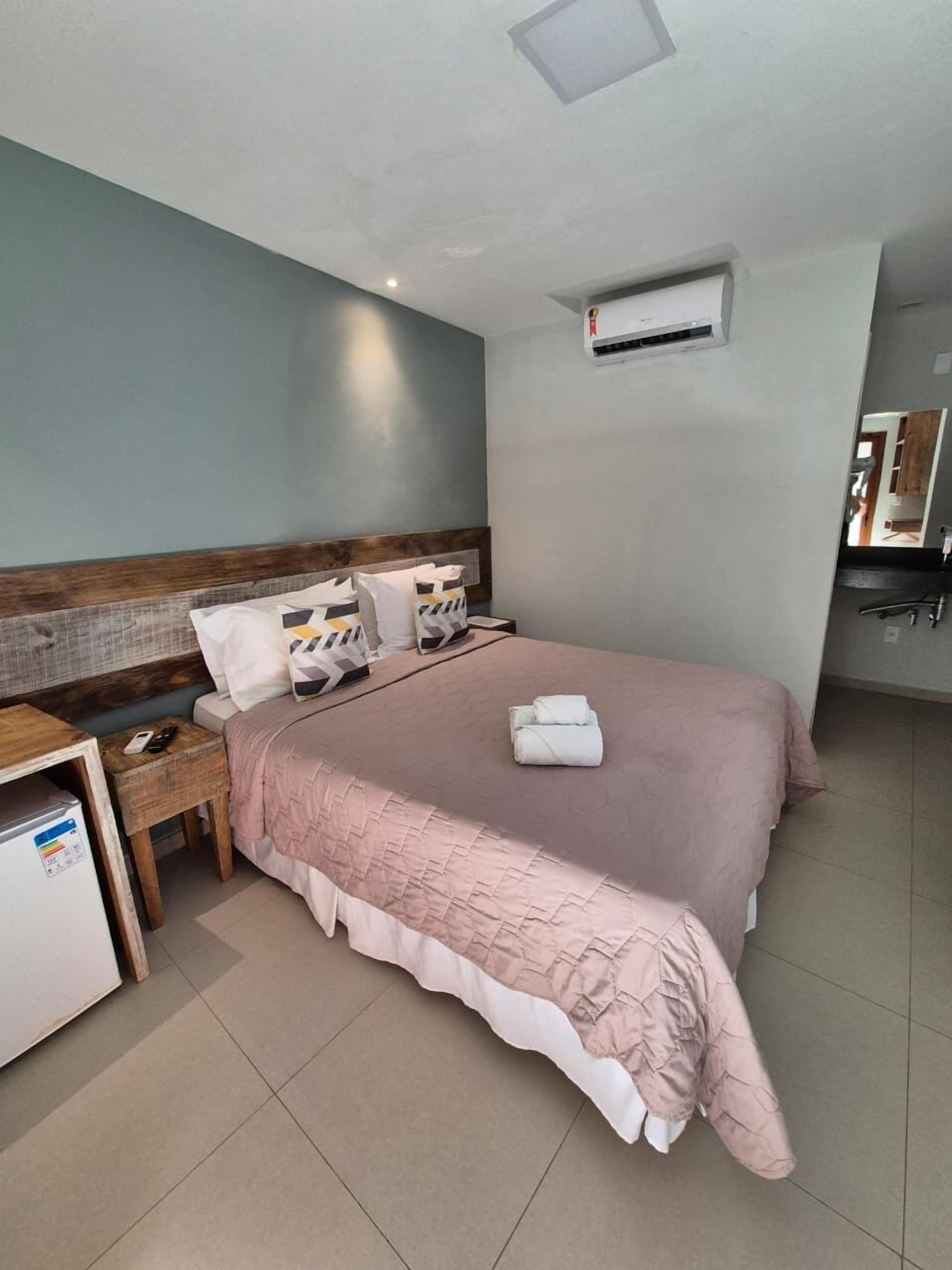 A neatly arranged hotel room with a bed, bedside table, and a small refrigerator.